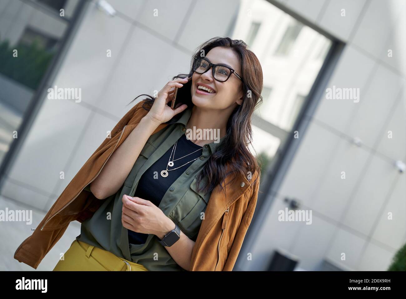 Buon colloquio. Giovane bella ed elegante donna che parla con uno smartphone con un amico e sorridente mentre si cammina per la strada della città. Concetto di stile di vita urbano, persone Foto Stock