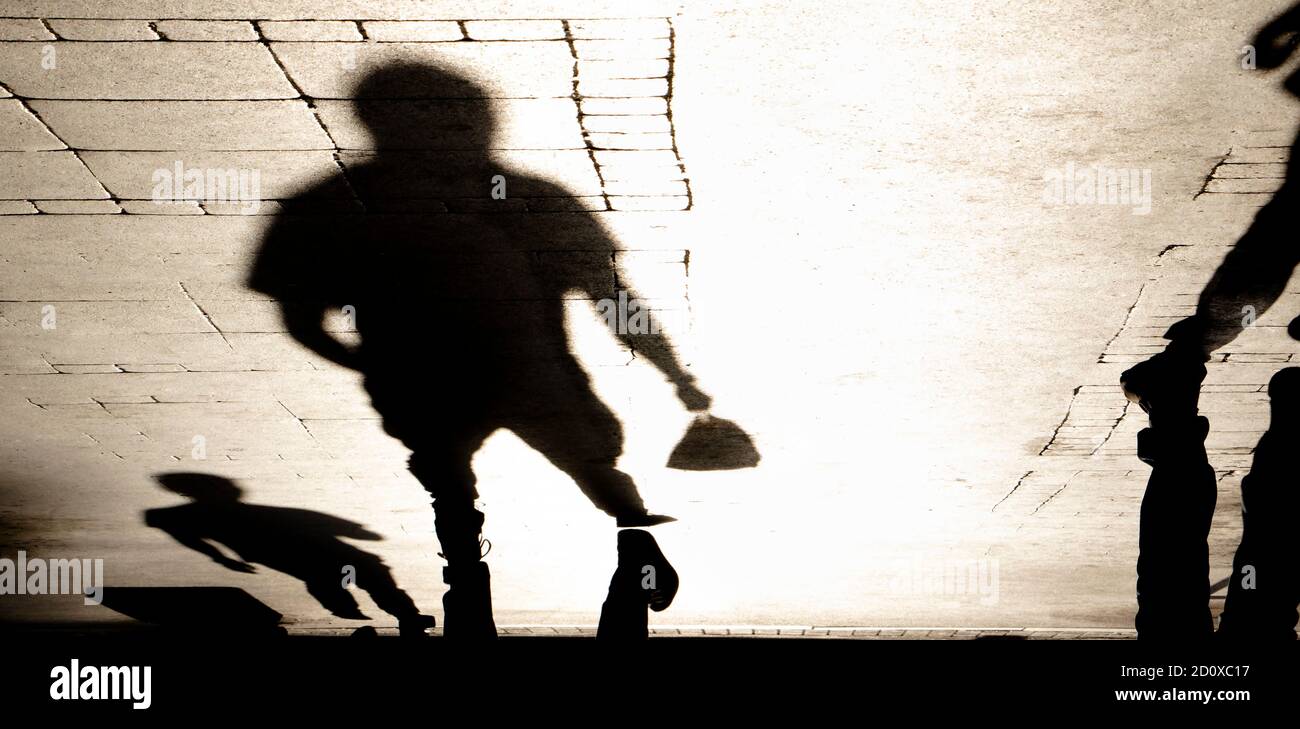 La silhouette ombra sfocata di uomini che camminano su strada pedonale che trasporta piccola borsa in seppia nera e bianca Foto Stock