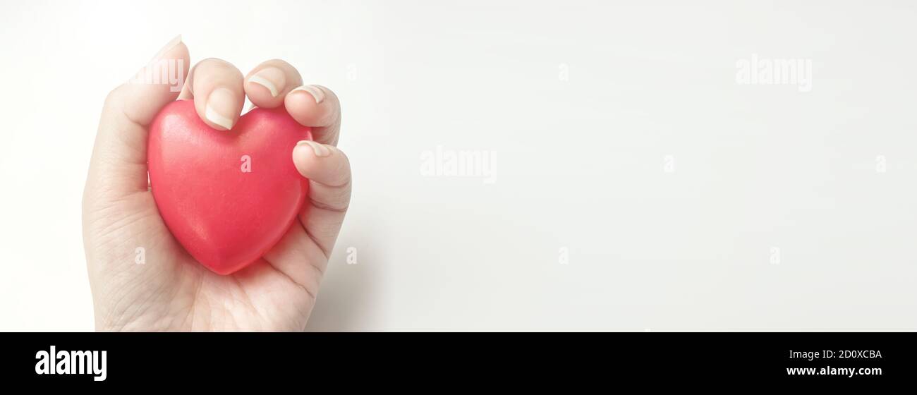 La mano della donna tiene il cuore rosso sullo sfondo bianco. Assicurazione sanitaria, donazione, concetto di salvataggio della vita. Idea giornata di salute del cuore del mondo Foto Stock