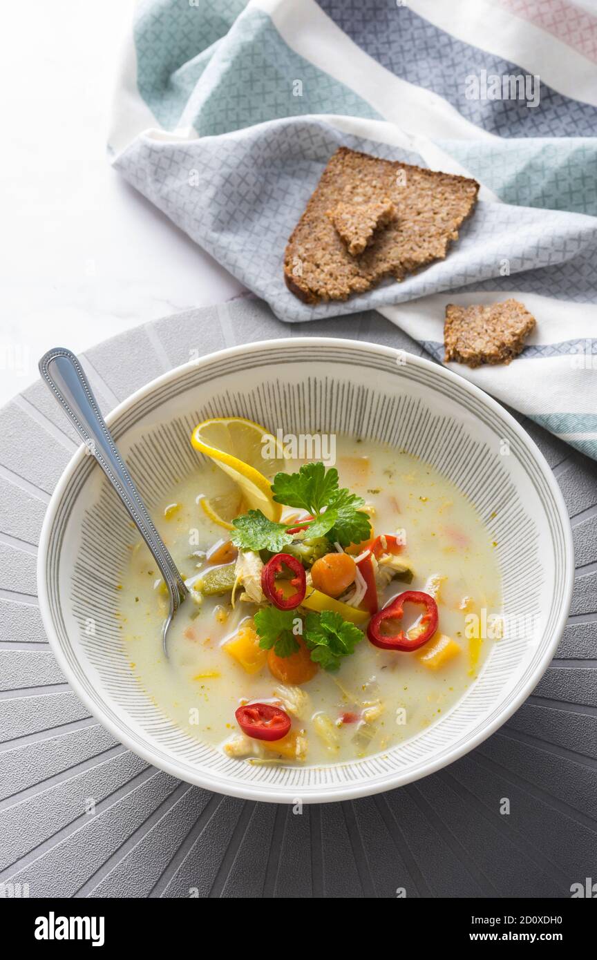 Zuppa rustica di pollo con verdure, tagliatelle, fettine di limone, foglie di sedano e peperoncino rosso fresco su sfondo marmoreo Foto Stock