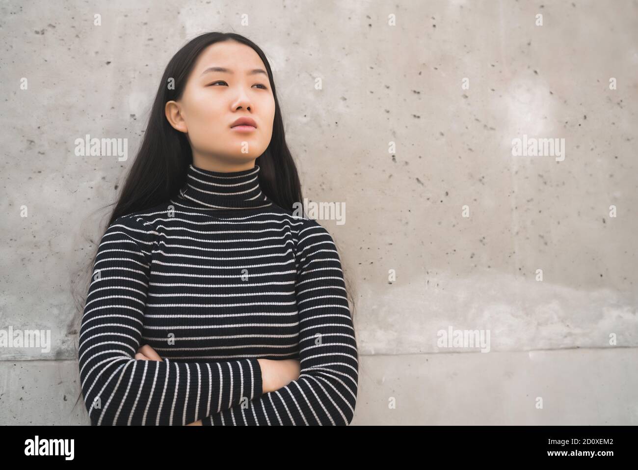 Ritratto di giovane bella donna asiatica in piedi all'esterno contro la parete grigia. Foto Stock
