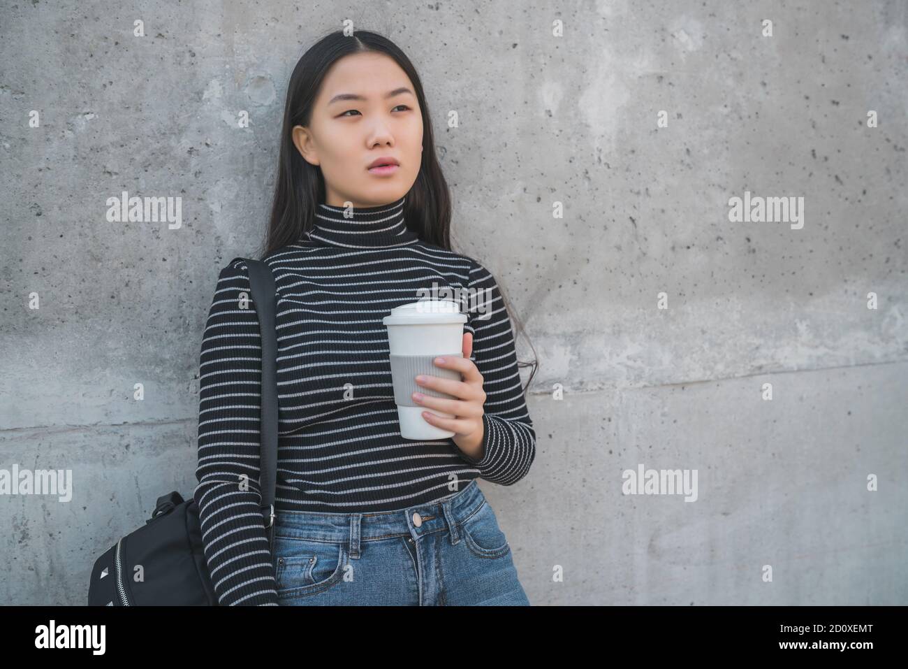 Ritratto di giovane donna asiatica in piedi all'aperto contro parete grigia. Foto Stock