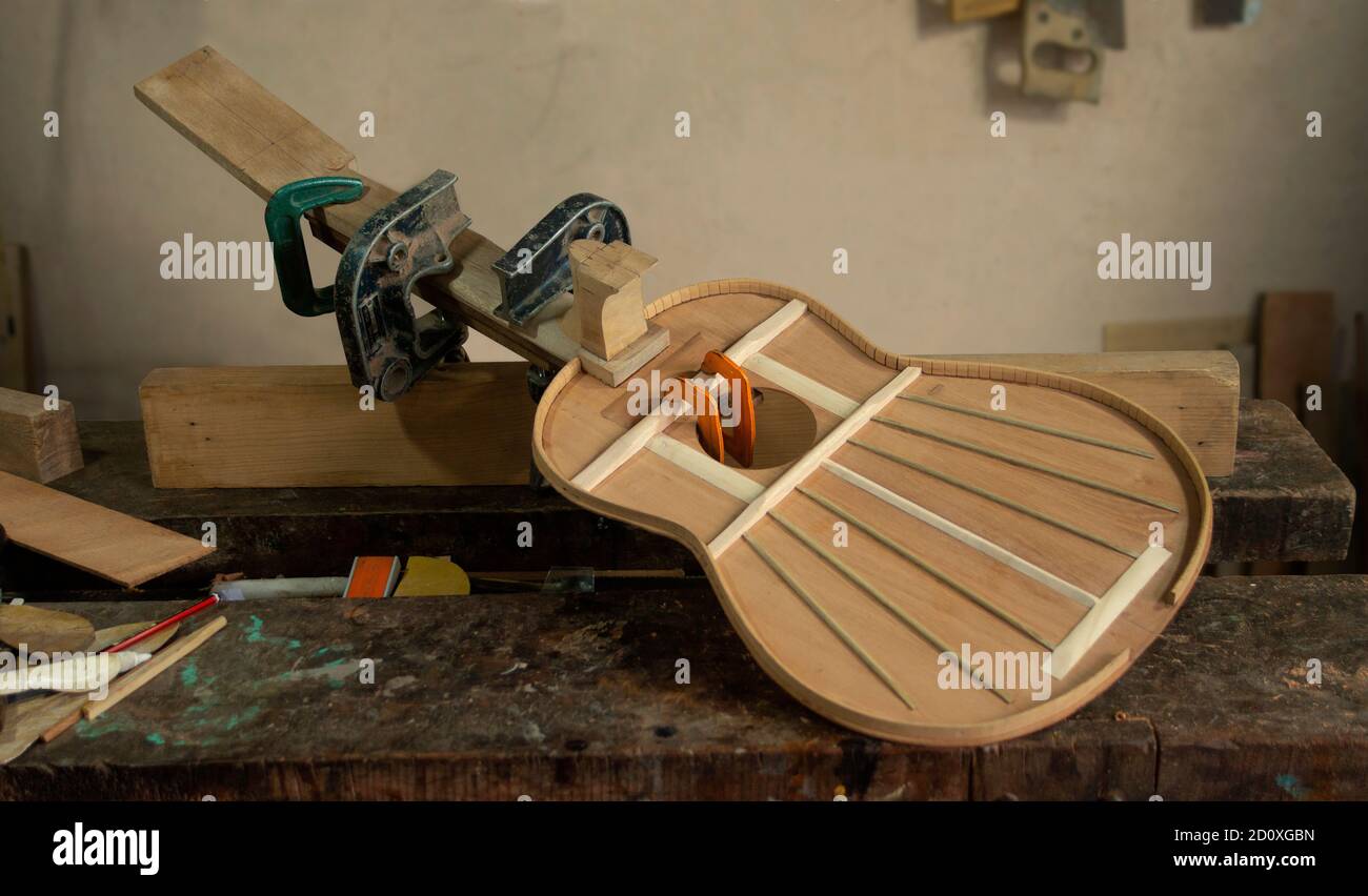 Chitarra di legno in processo di assemblaggio con presse che tengono le parti sopra banco da lavoro del falegname con parete grigia sullo sfondo Foto Stock