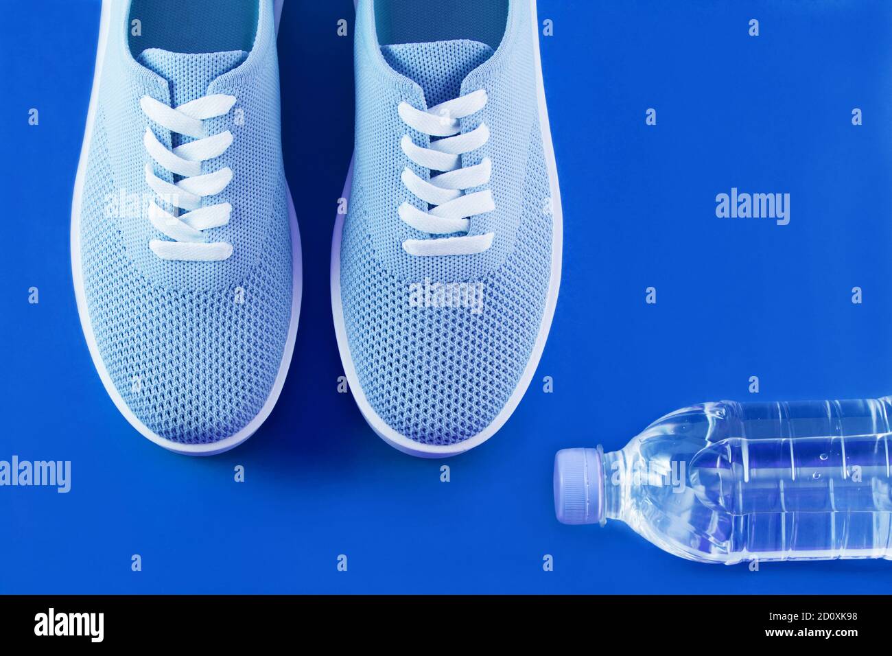 Formato su un brillante sfondo blu - la luce blu sneakers e una bottiglia di acqua su uno sfondo blu con un posto per un'iscrizione. Foto Stock