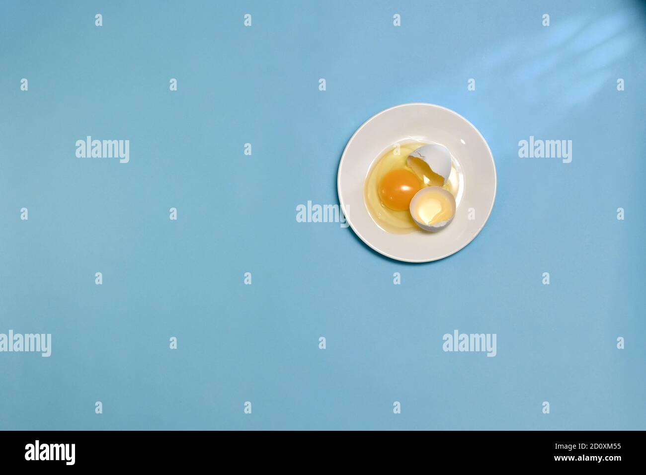 Uovo crudo bianco di pollo spezzato, completo di semigusci, con proteina sparsa e tuorlo giallo, nel piatto bianco. Foto Stock