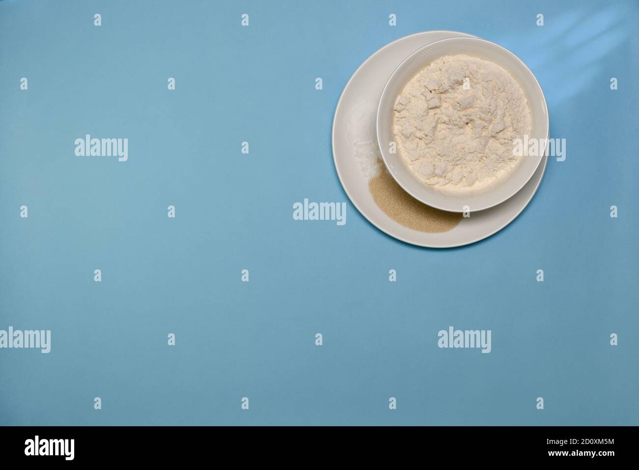 Alcuni degli ingredienti per l'impasto cucinati in piatti bianchi. Farina sale di lievito e lievito in polvere. Su sfondo blu. Foto Stock
