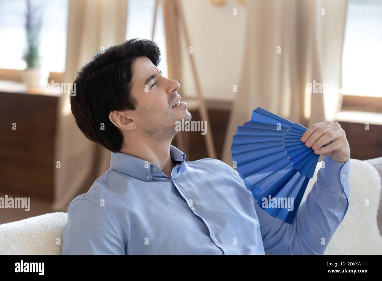 Male infelice rilassarsi all'interno senza aria condizionata con ventilatore a mano Foto Stock