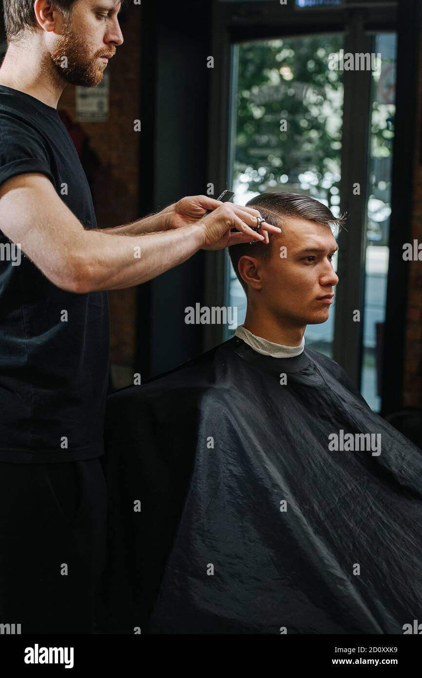 Parrucchiere maschile con lappatura stretta che fa un taglio di capelli per un giovane uomo in un barbiere Foto Stock