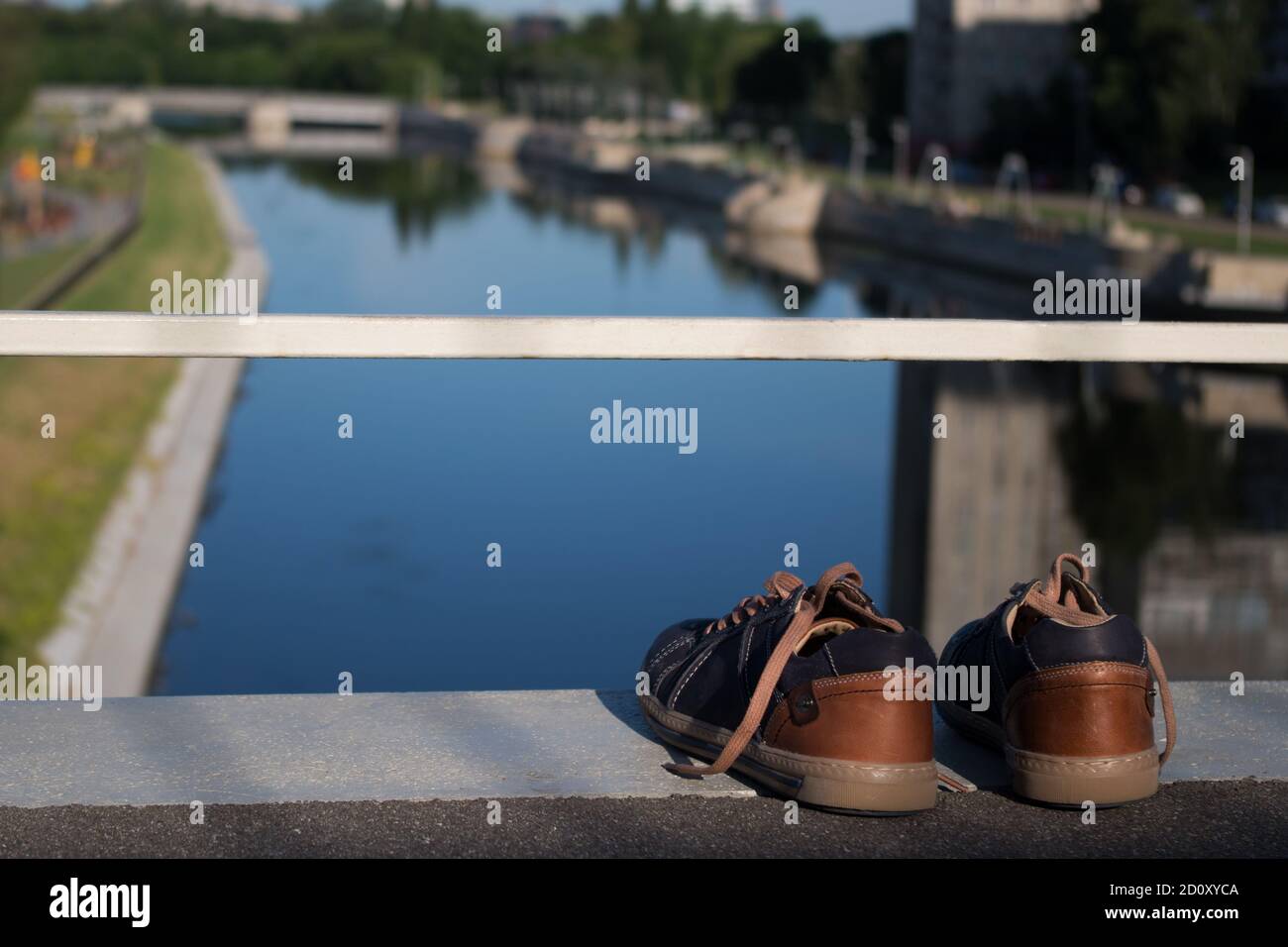 Un paio di sneaker da donna in piedi contro una ringhiera bianca sul bordo del ponte sul fiume urbano blu sottostante, vista dalla cima del ponte Foto Stock