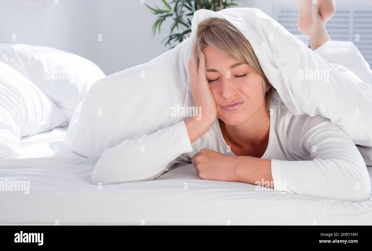 bella giovane donna in letto bianco al mattino, non vuole svegliarsi. Sonno insufficiente. Foto Stock