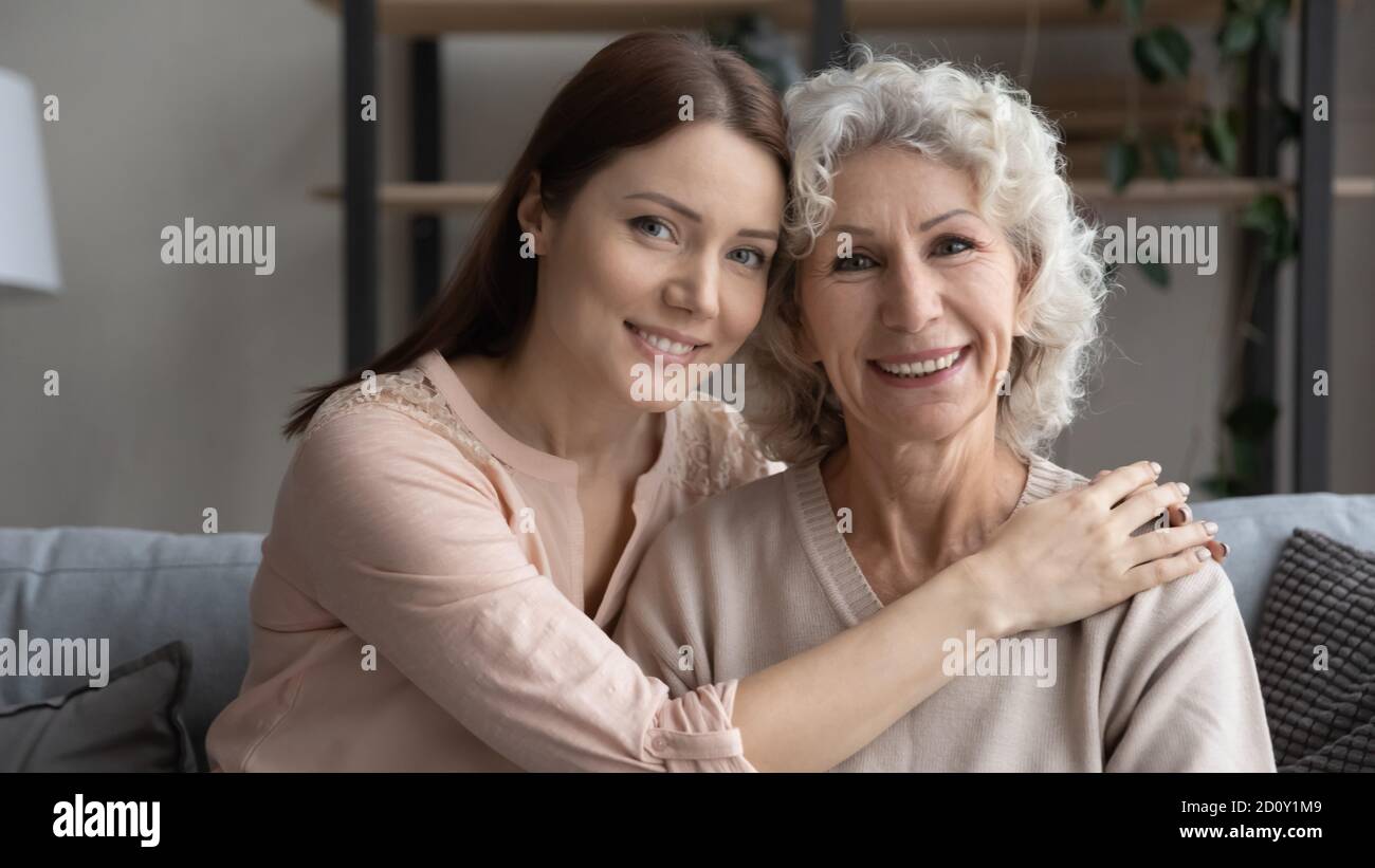 La testa ha girato sorridendo la giovane donna con la madre anziana abbracciando Foto Stock