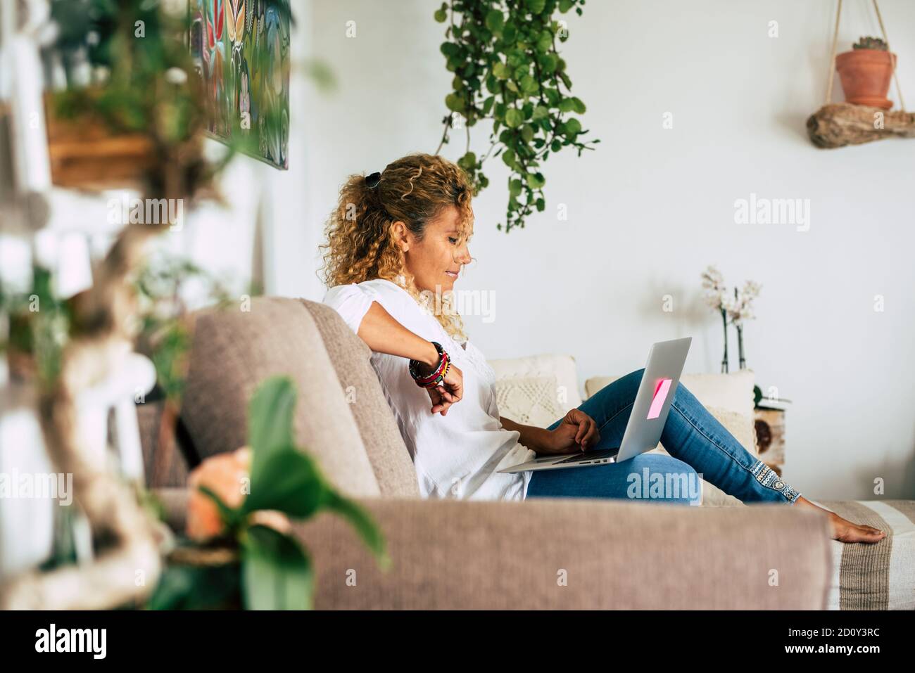Stile di vita domestico scena reale con le persone e la tecnologia .- bella donna si siede sul divano e usa un computer portatile e la connessione per il lavoro o guardare f Foto Stock