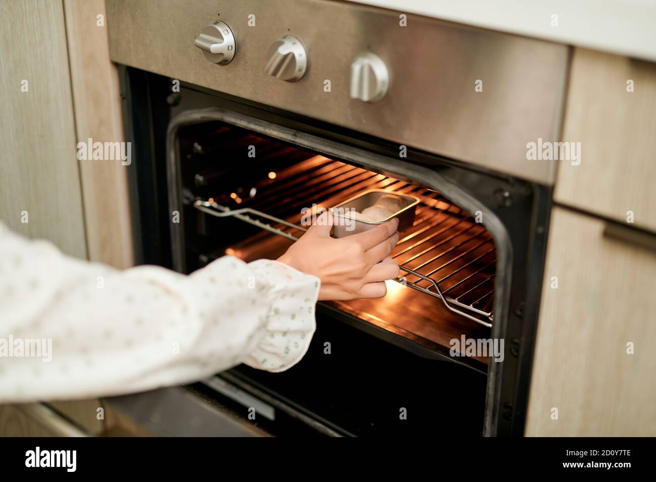 donna che indossa il forno mitt mettendo teglia con biscotti crudi in forno moderno in cucina domestica Foto Stock