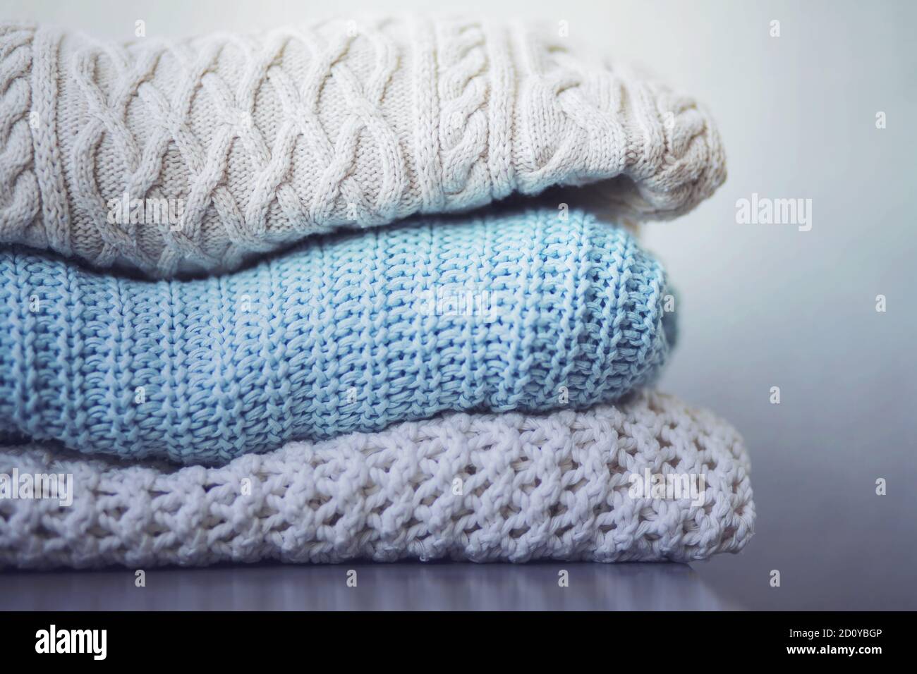 Sul tavolo grigio, tre pullover di lana calda con diversi modelli sono impilati in un palo, pronti per il freddo. Periodo invernale. Foto Stock