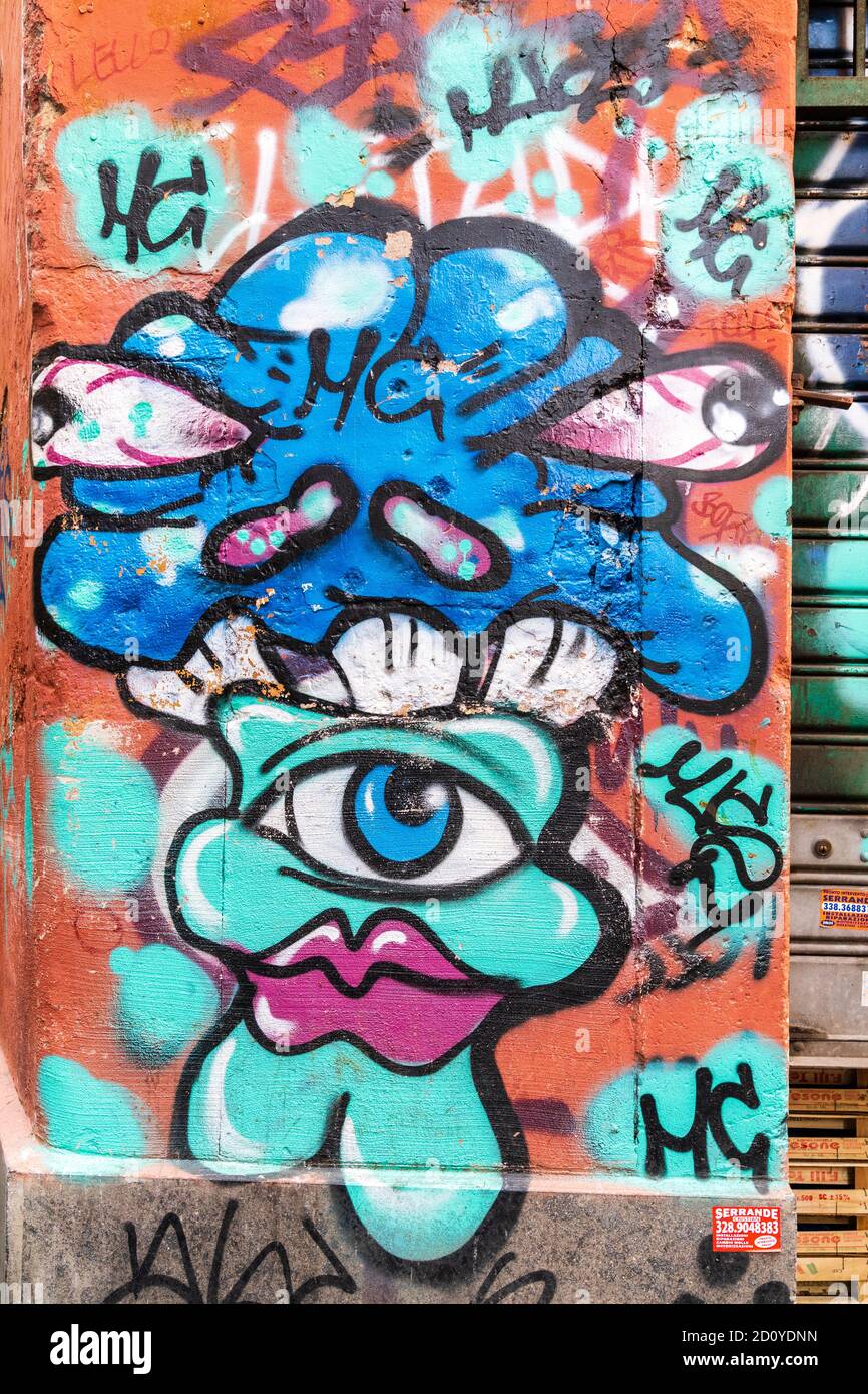 Graffiti su un muro a Roma. Con un viso turchese con labbra rosa e un occhio con forma blu sopra con due occhi che si stagliano. Foto Stock