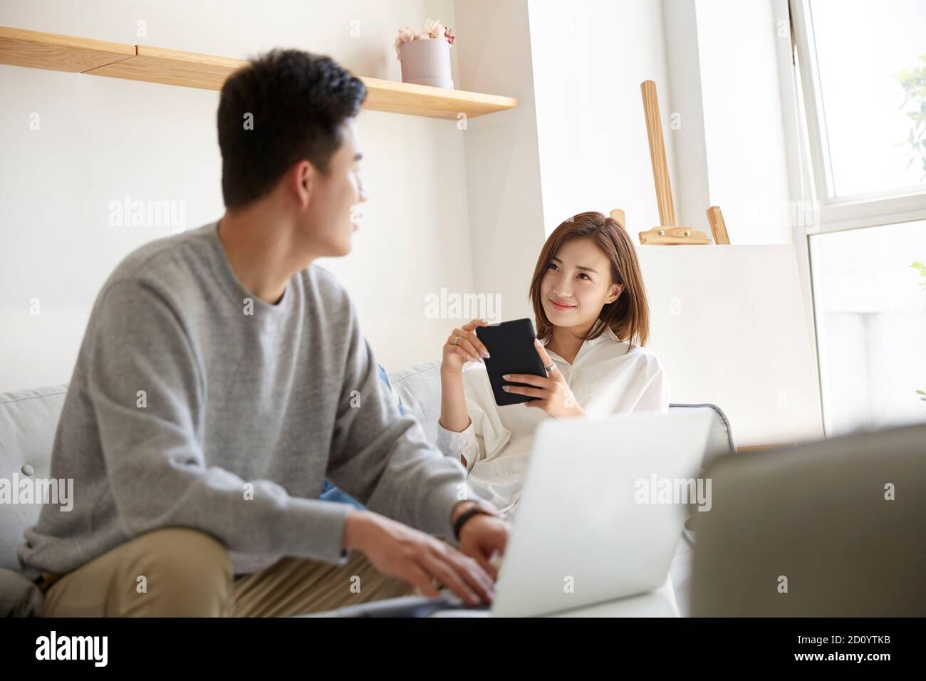 felice e rilassata giovane coppia asiatica che chiacchiera mentre si soggiorna a casa Foto Stock