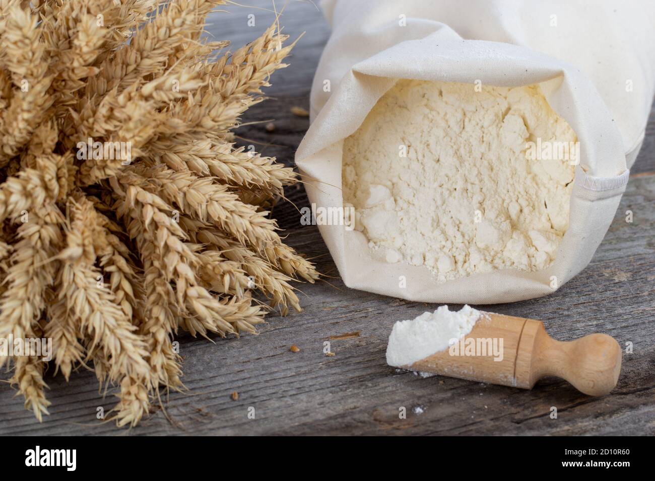 Sacco di farina, orecchie e misurino in legno su fondo di legno. Prodotti da forno naturali. Foto Stock