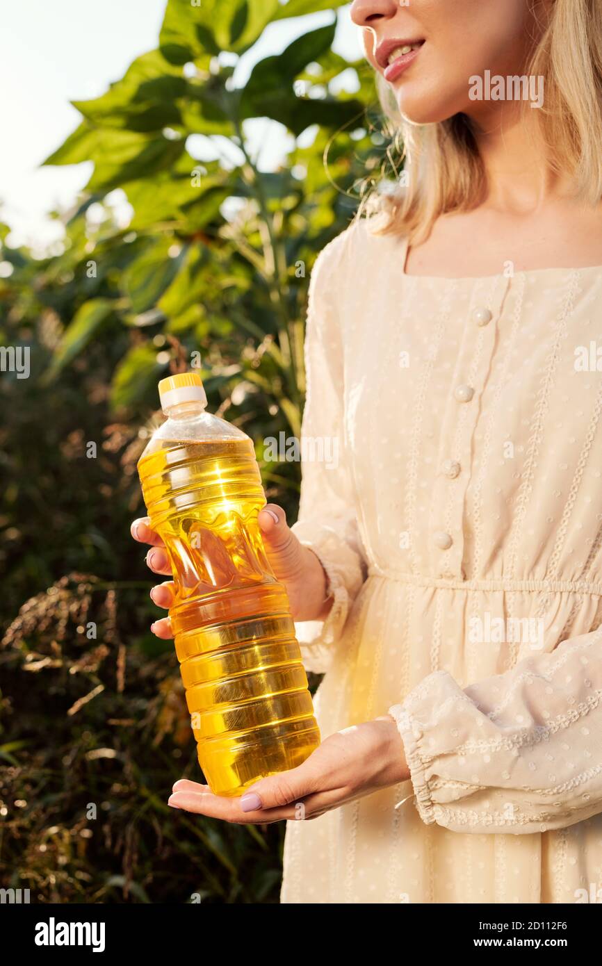 Giovane donna bionda in elegante abito bianco che tiene una bottiglia di olio di girasole Foto Stock