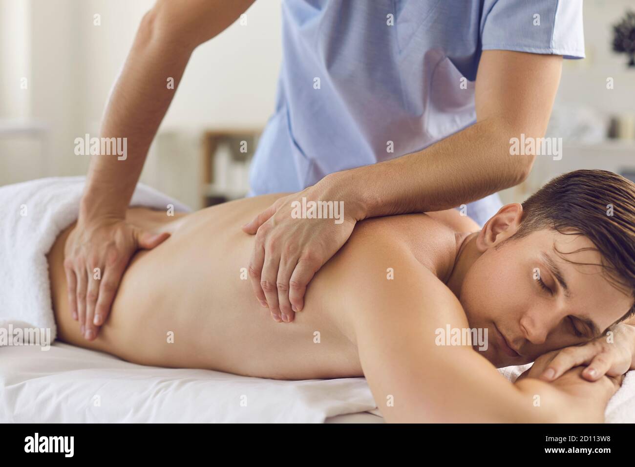 Rilassato giovane uomo godendo di massaggio terapeutico corpo fatto da professionista massaggiatore Foto Stock