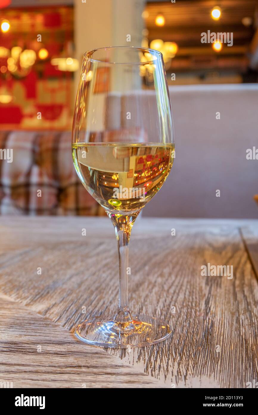 Un bicchiere di vino bianco si erge su un tavolo con una superficie in legno in un caffè. Orientamento verticale, messa a fuoco selettiva, sfondo sfocato. Foto Stock