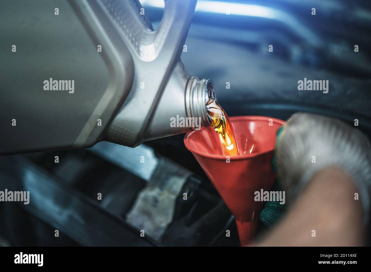 Il lavoratore versa il nuovo olio motore sintetico dal canister nell'imbuto durante il servizio di assistenza auto, cambio olio regolare - concetto di salute auto. Foto Stock