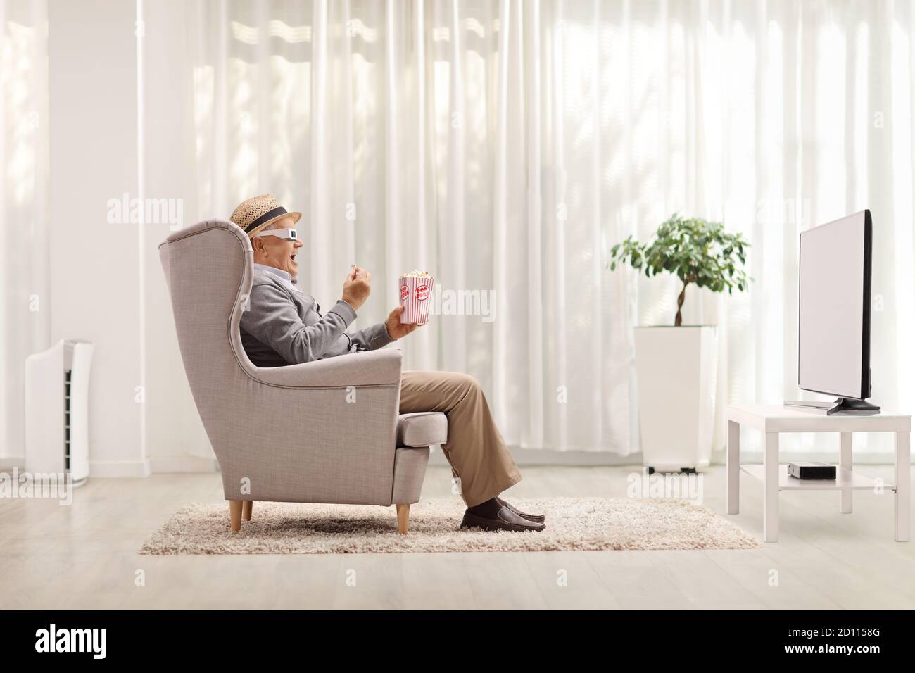 Uomo maturo con occhiali 3D che guardano un film a casa e tenendo una scatola di popcorn Foto Stock