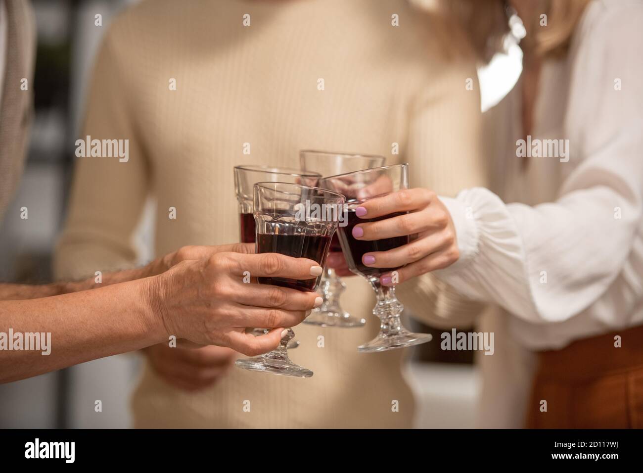 Le mani di quattro membri della famiglia in casualwear che si aggraffano con gli occhiali di vino rosso Foto Stock