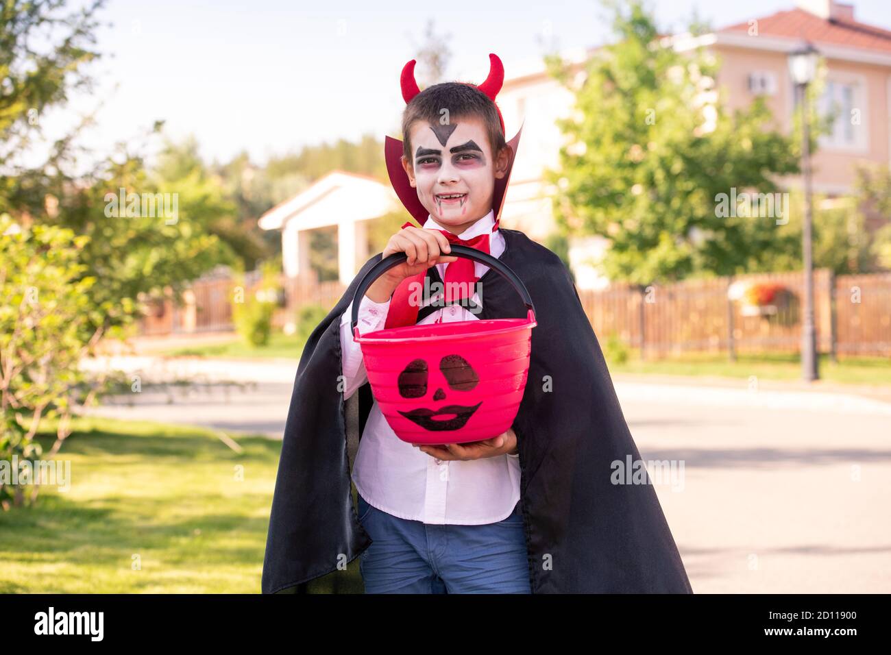 Ragazzo allegro in costume halloween di diavolo con corna su la sua testa che tiene le delizie Foto Stock