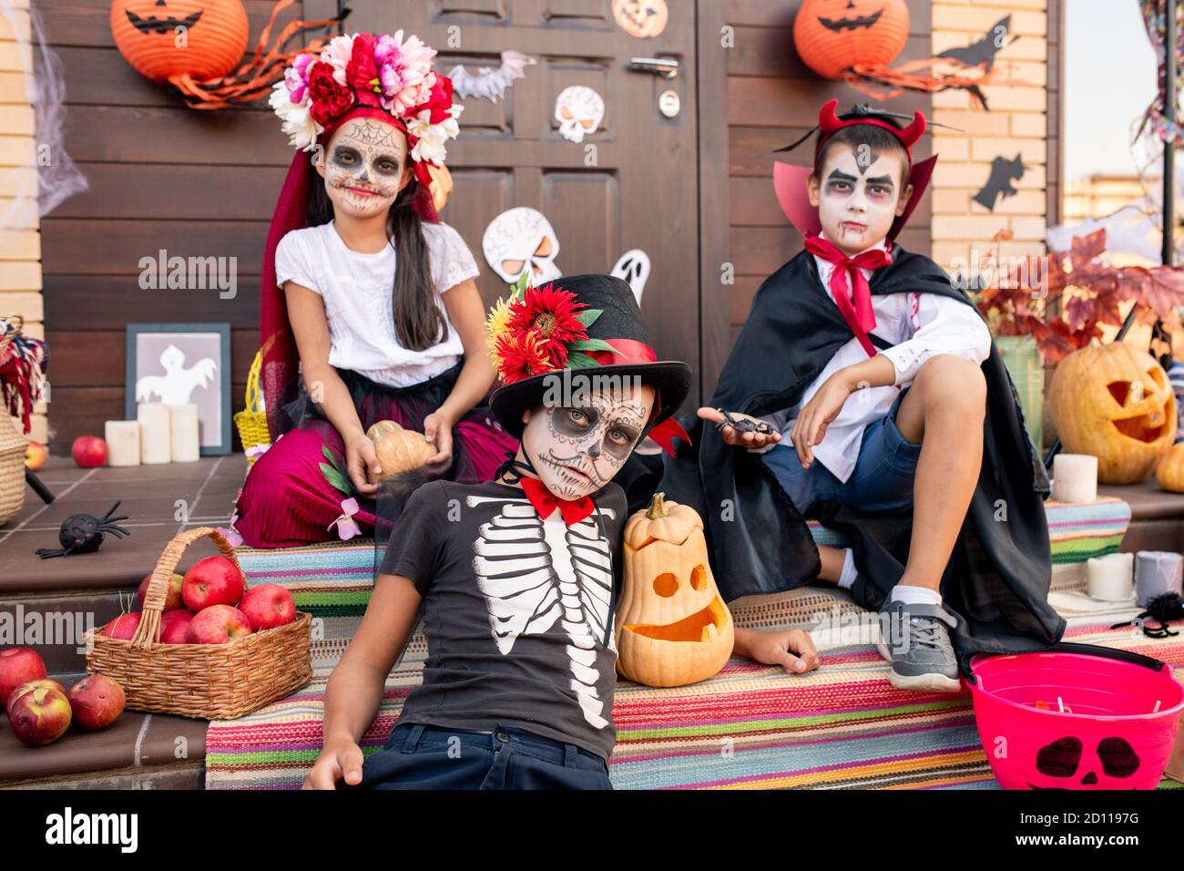 Ragazzo cupo con il volto dipinto che ti guarda mentre sei seduto dai suoi due amici Foto Stock