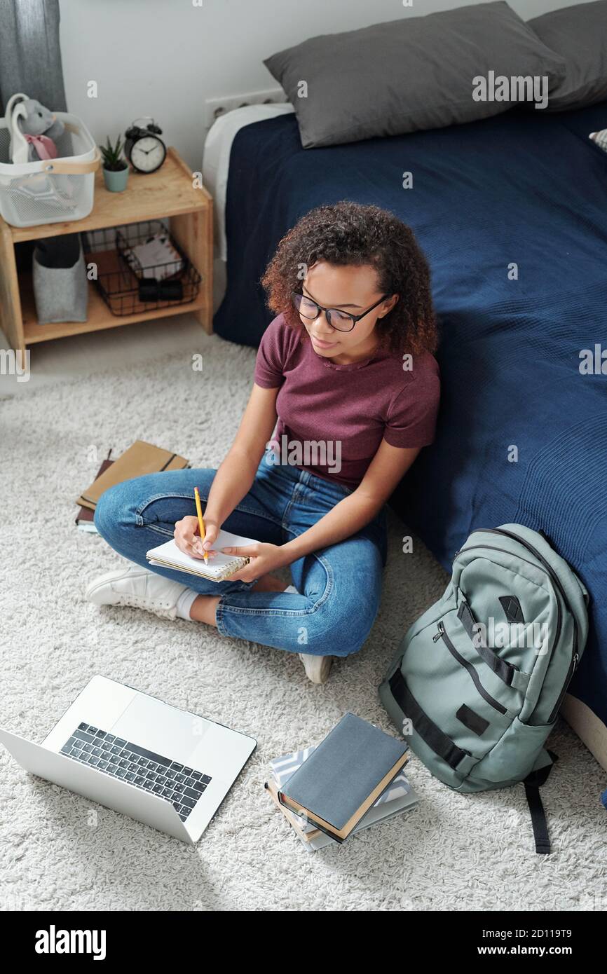 Giovane studente contemporaneo seduto di fronte al computer portatile e fare note Foto Stock