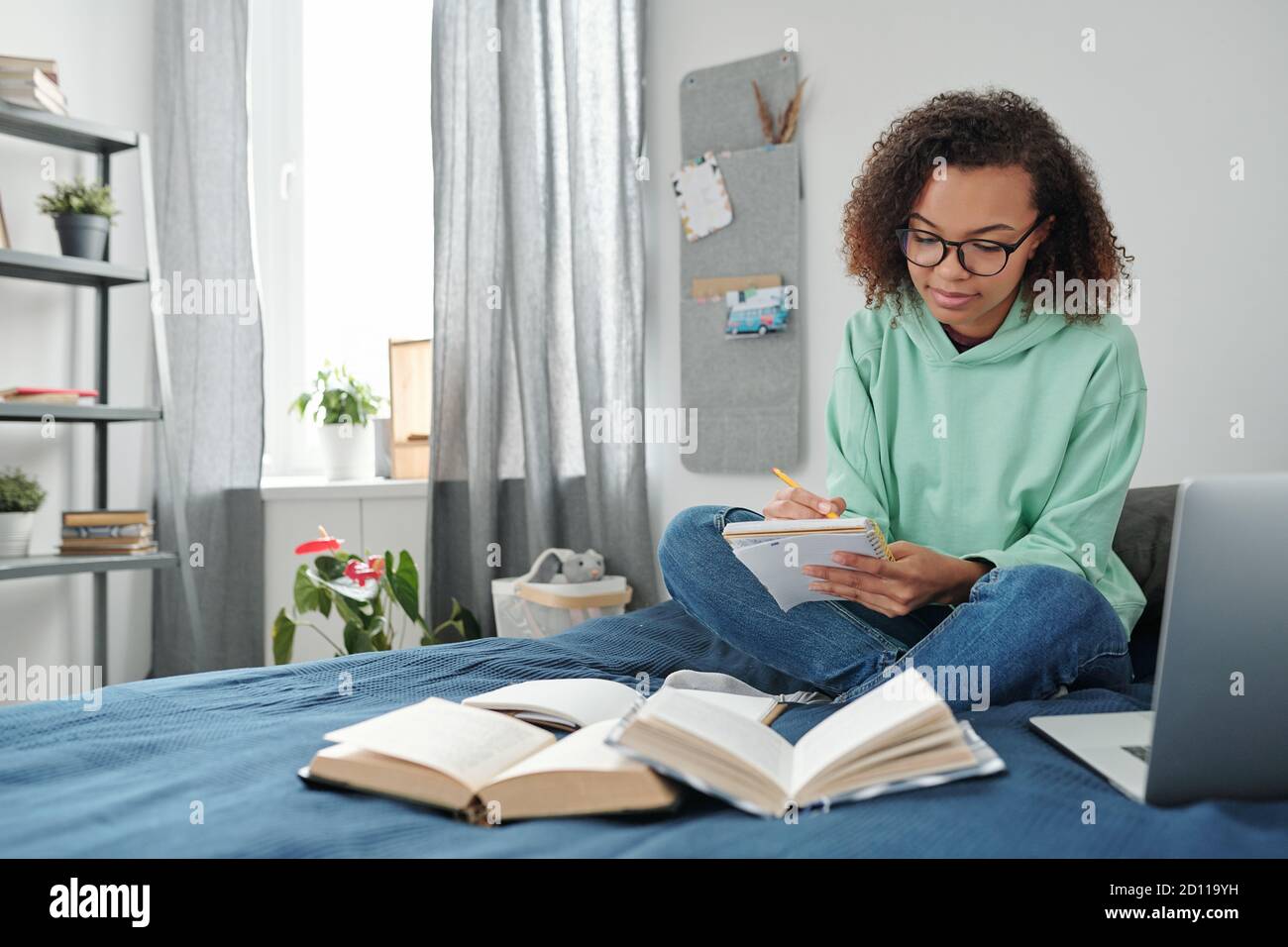 Giovane studente diligente di razza mista in casualwear facendo note in copybook Foto Stock