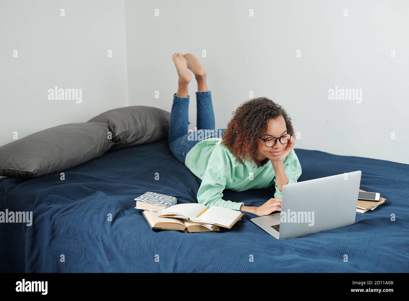 Giovane studentessa rilassata in jeans e felpa con cappuccio che si prepara per prossimi esami Foto Stock