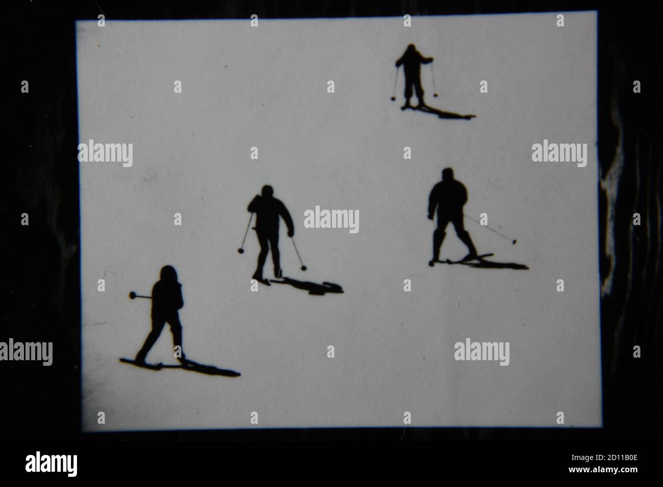 Fine anni '70 vintage profilo in bianco e nero fotografia di sciatori sulla collina di sci nei loro completi abiti da sci e sci che scende la collina. Foto Stock