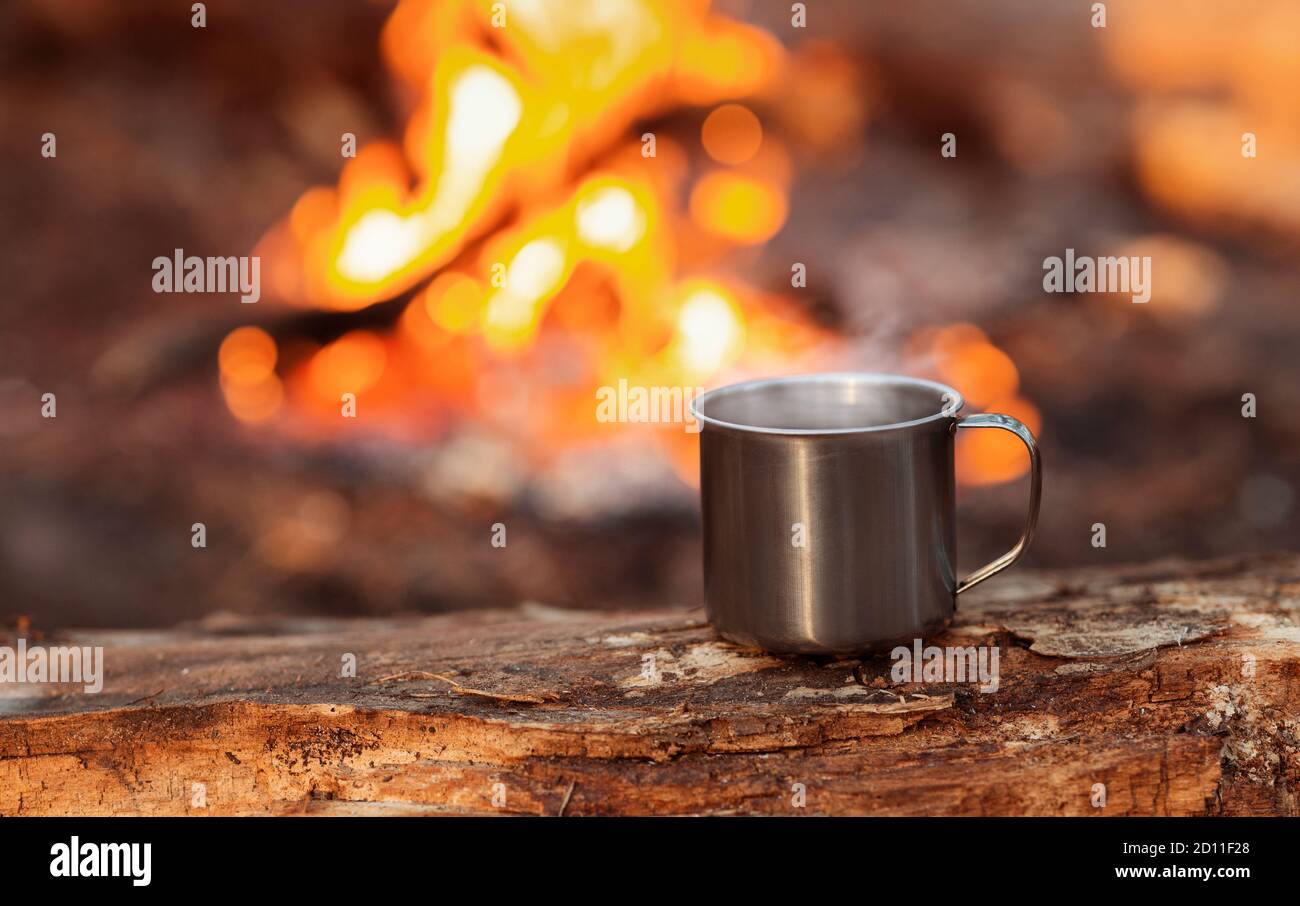 Tazza di campeggio su legno su sfondo fuoco Foto Stock