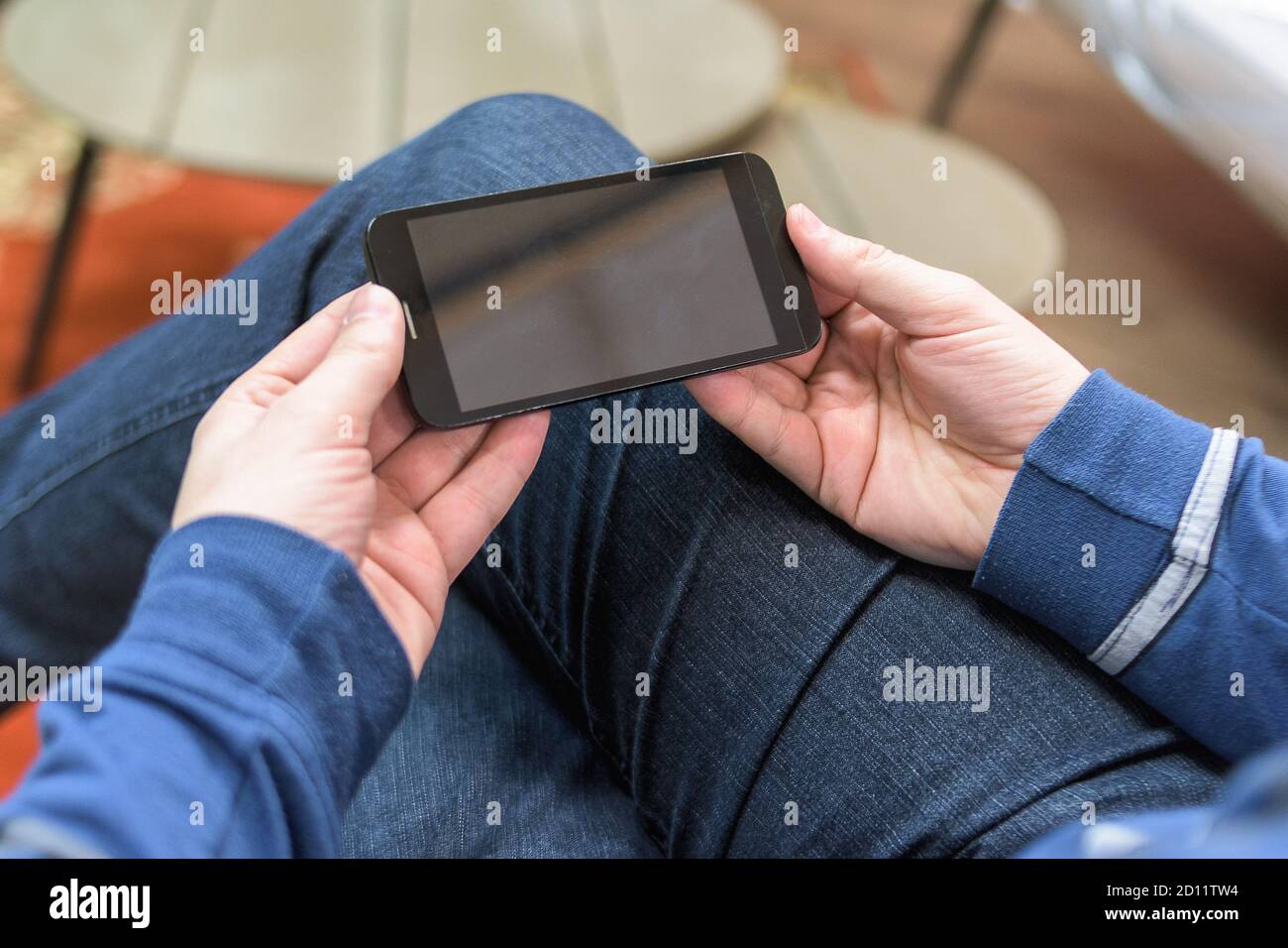 Primo piano foto uomo tenere e guardare video cellulare. Uomo seduto in sedia vintage, tenendo smartphone e rilassante.orizzontale, effetto film. Man entr Foto Stock