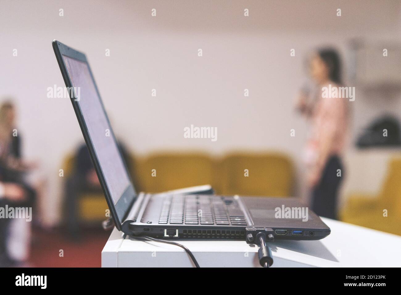 Computer portatile su banco di presentazione aziendale con persone arrossate in background bokeh. Foto Stock