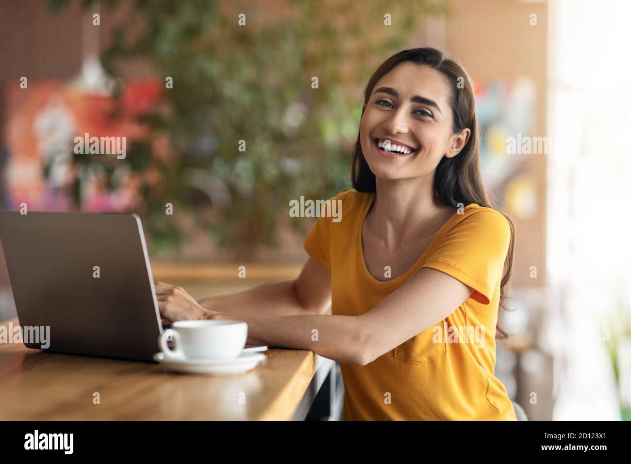 Allegra signora araba seduto davanti al computer portatile al bar Foto Stock
