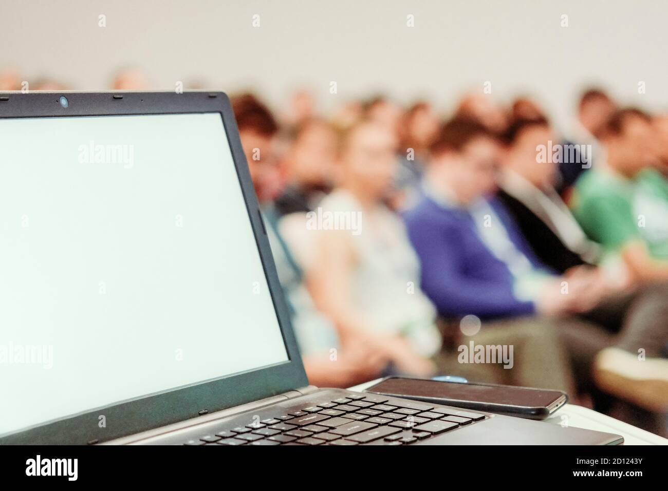 Computer portatile su banco di presentazione aziendale con persone arrossate in background bokeh. Foto Stock