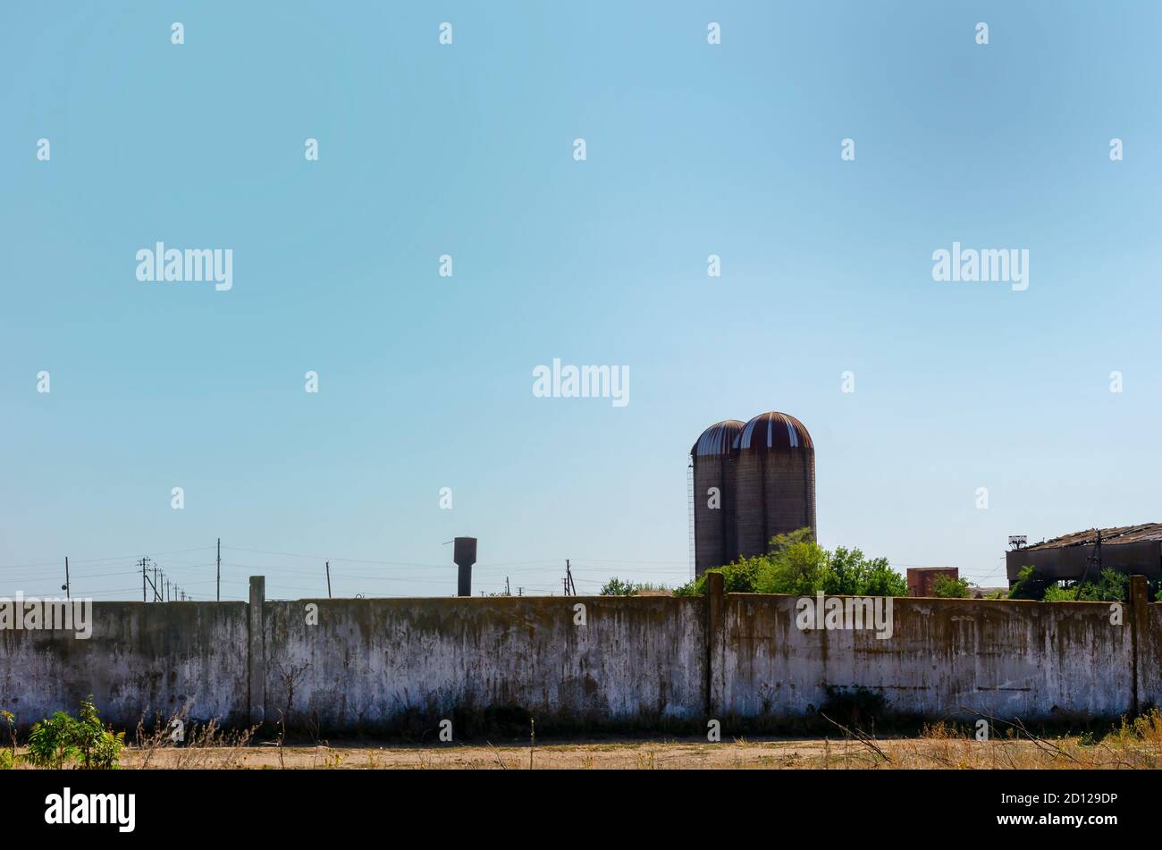 L'area abbandonata di un antico granaio con alti silos cilindrici in pietra. Questo complesso edilizio molto vecchio e fatiscente è circondato da una recinzione in cemento. Foto Stock