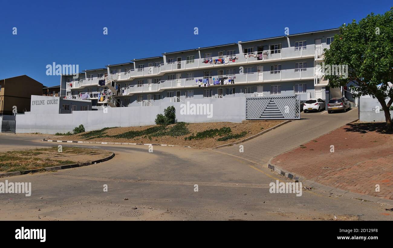 Windhoek, Namibia - 05/05/2018: Casa plurifamiliare protetta dipinta di grigio chiamata 'Eveline Court' ai margini della cittadina Katutura con strada. Foto Stock