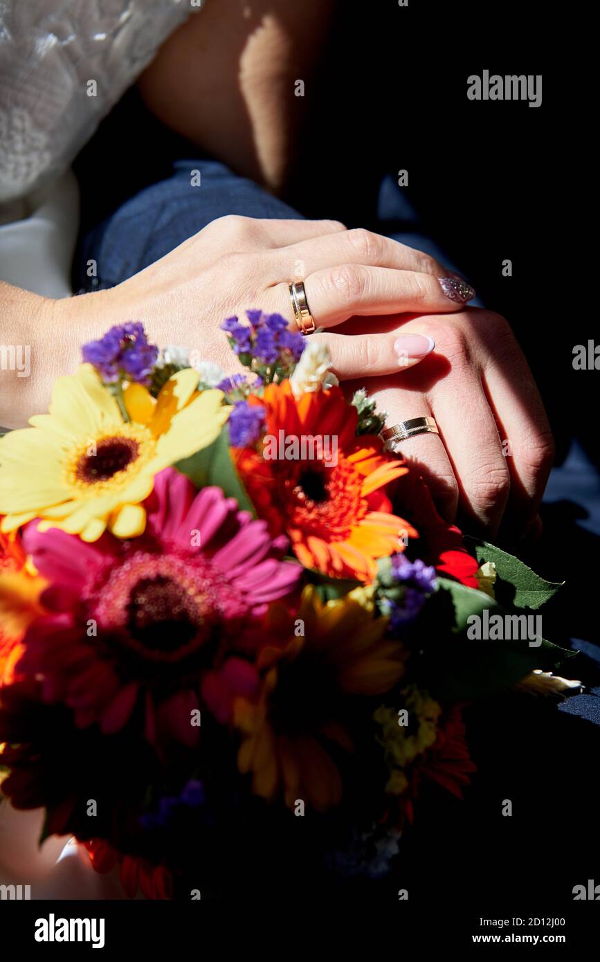 Mani della sposa e dello sposo con anelli di nozze vicino ad un mazzo di fiori. Foto Stock