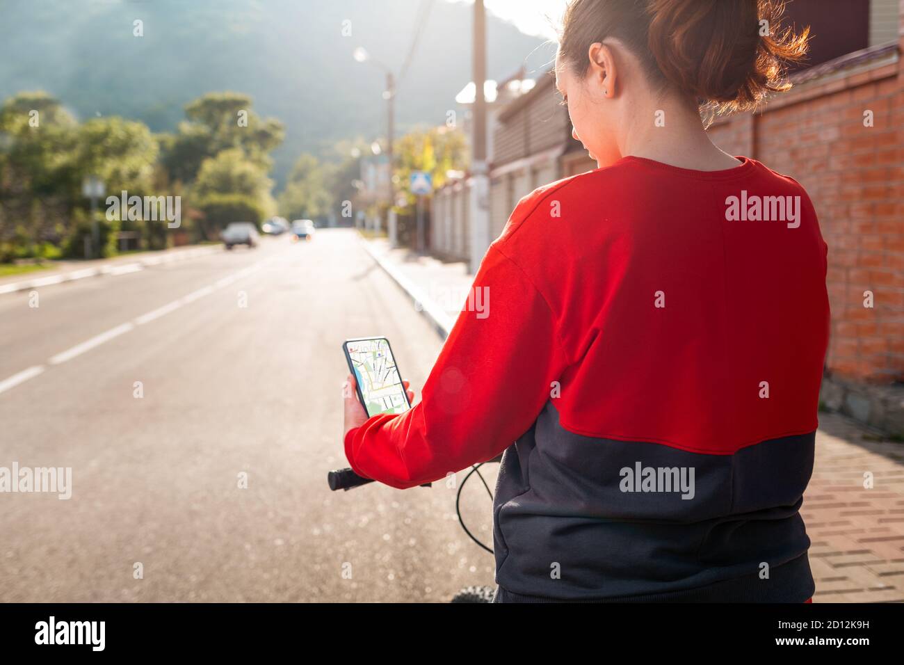 Una donna ha uno smartphone con un'app mappa online. Vista posteriore. Sullo sfondo c'è una strada cittadina. Il concetto di navigazione Internet e tecnologia moderna Foto Stock