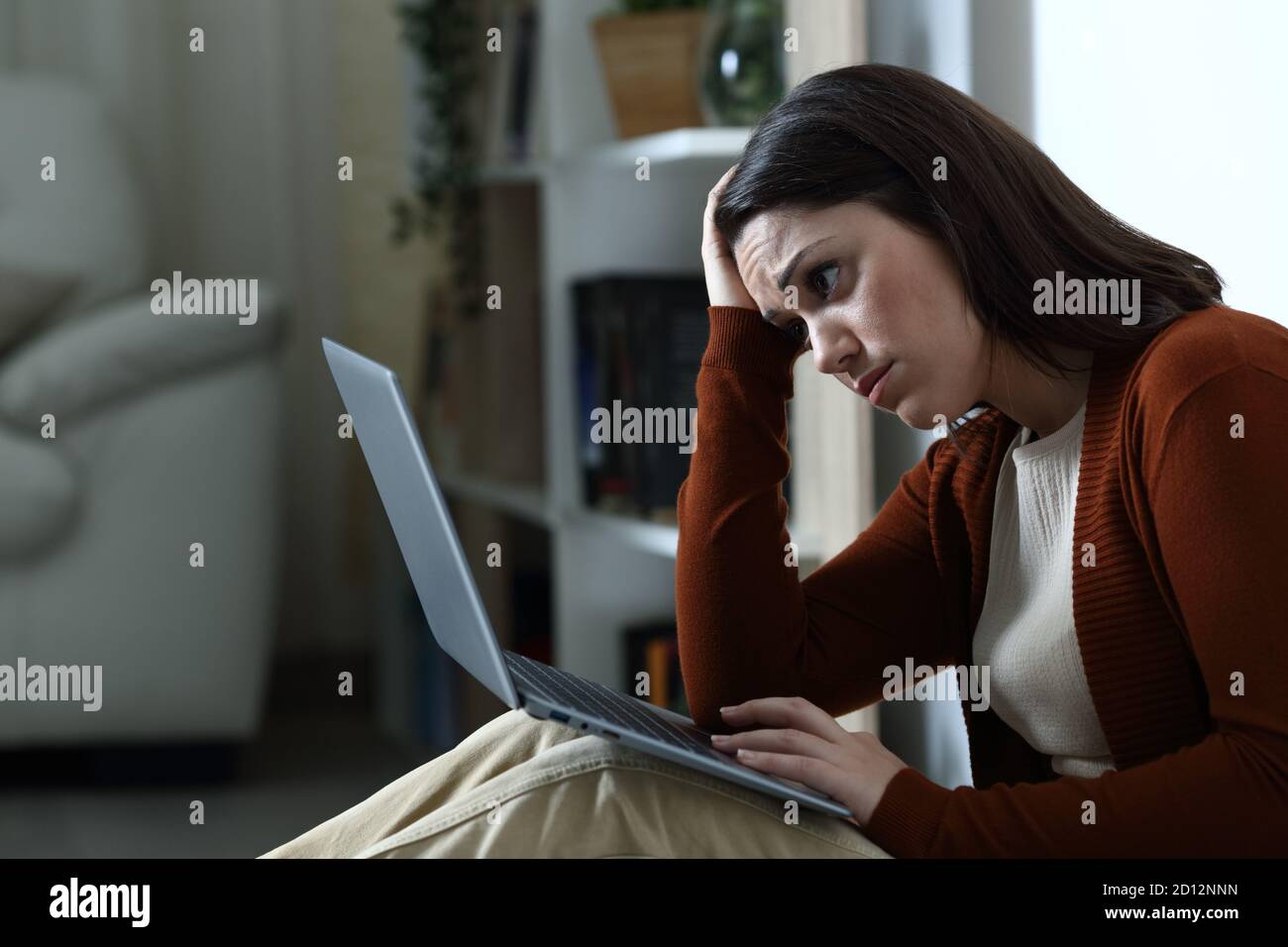 Triste donna che controlla cattive notizie sul laptop a casa in la notte Foto Stock