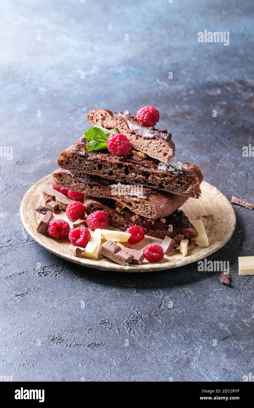 Fette di dolci fatti in casa il dessert cioccolato pizza con diversi cioccolatini, lamponi e menta servito sulla piastra in ceramica blu su sfondo di texture. Co Foto Stock