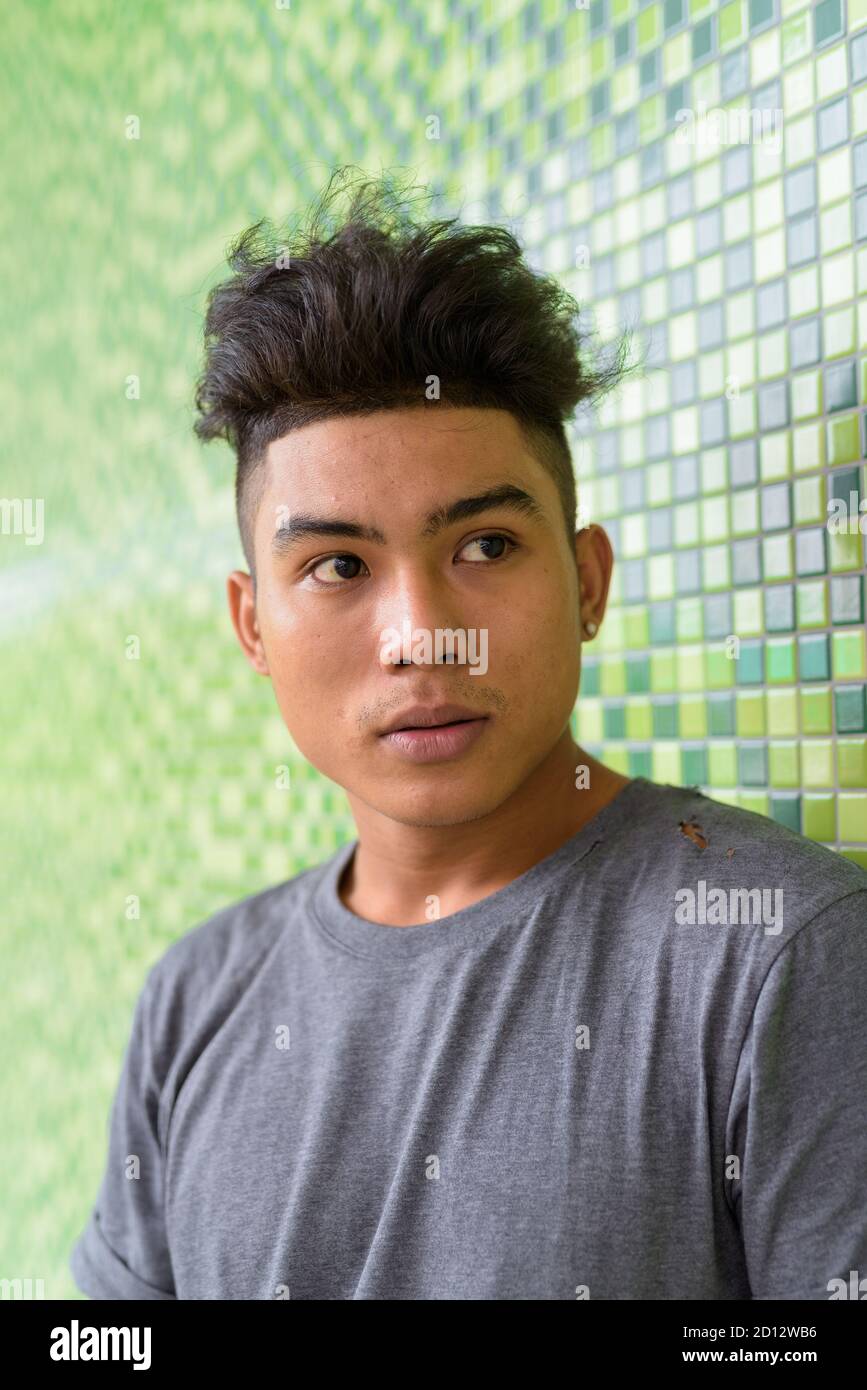 Volto di giovane uomo asiatico con capelli ricci che pensano contro parete verde all'aperto Foto Stock