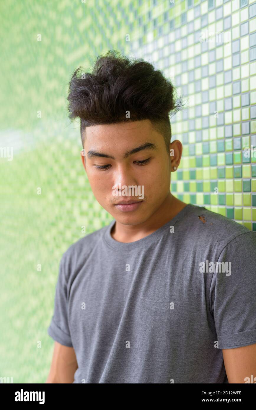 Volto di giovane asiatico con capelli ricci che guardano verso il basso contro parete verde all'aperto Foto Stock