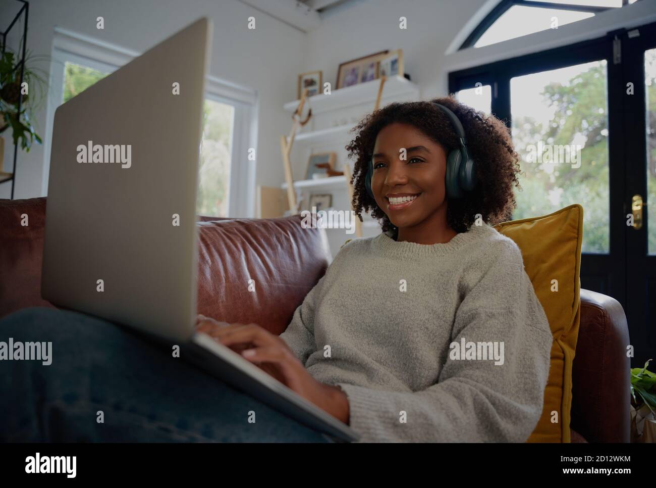 Giovane donna africana allegra che si rilassa a casa guardando serie web con le cuffie sedute sul divano Foto Stock