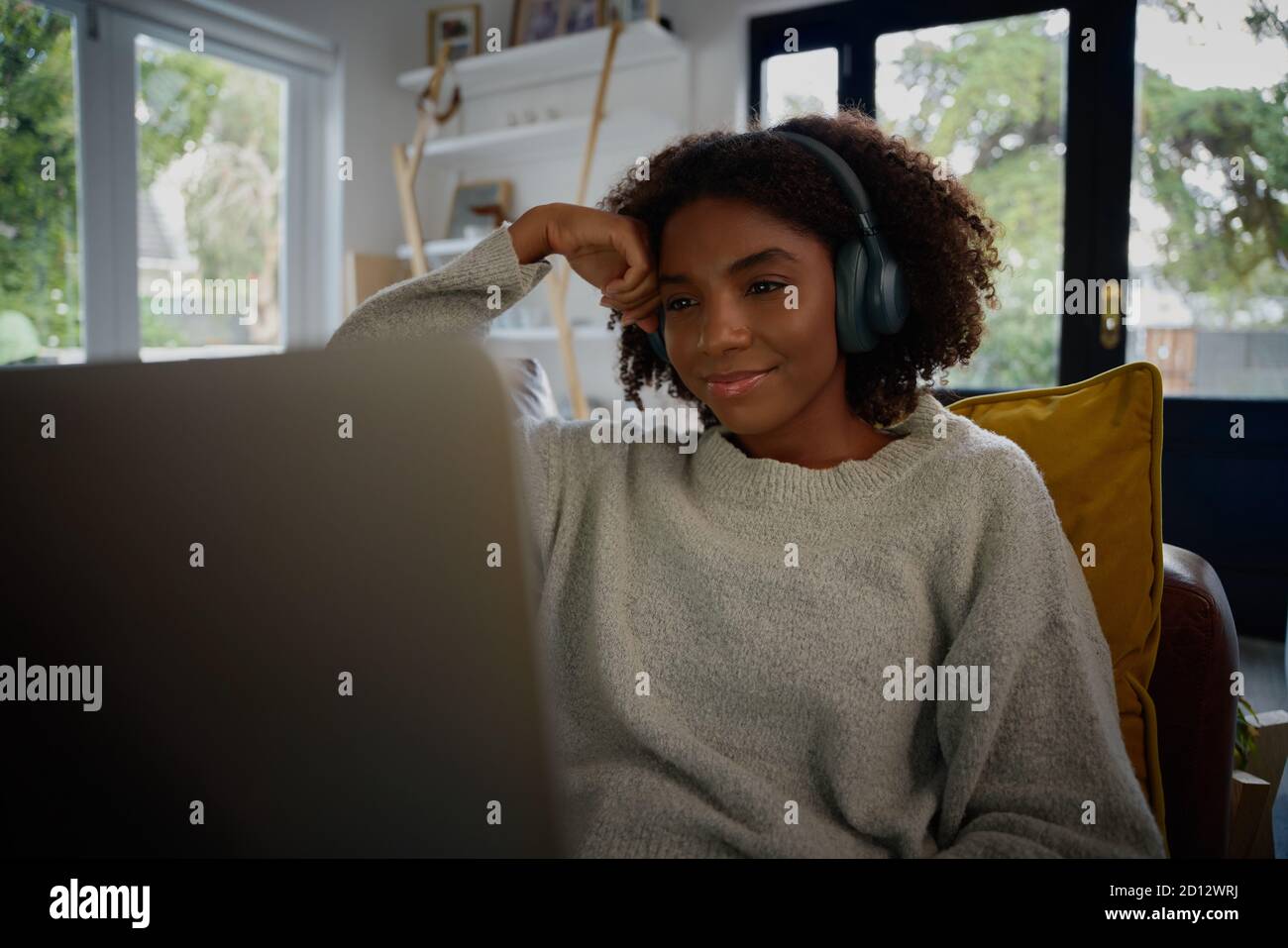 Una giovane donna africana sorridente che guarda il webinar su un computer portatile con cuffie a casa Foto Stock