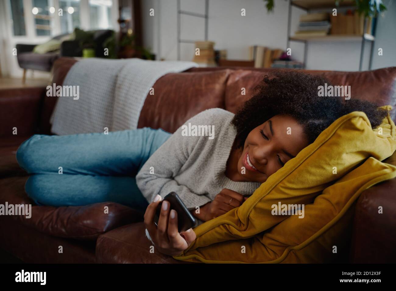 Giovane donna allegra che sorride mentre guarda il video sullo smartphone sdraiato sul lettino Foto Stock