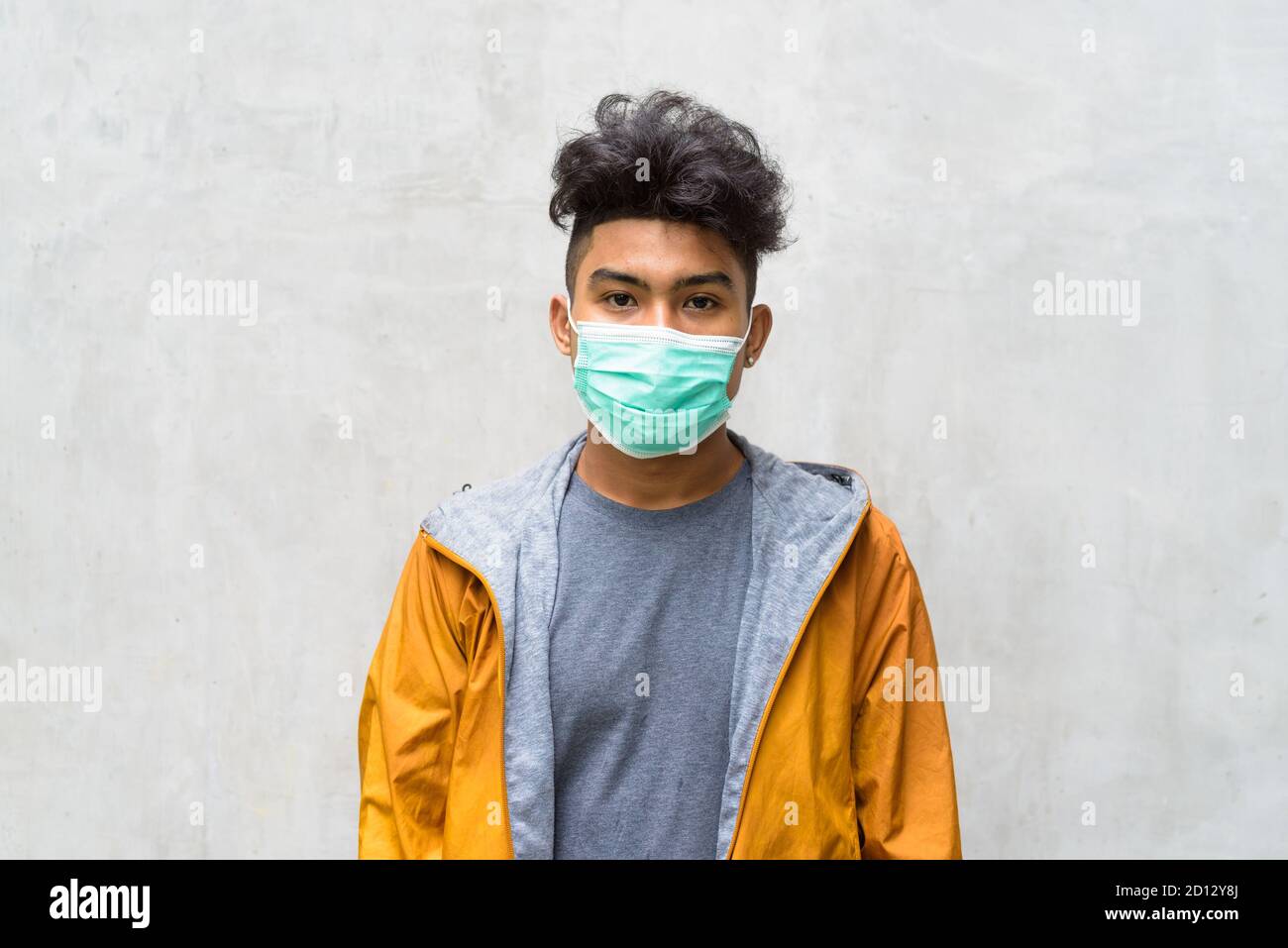 Giovane asiatico con capelli ricci che indossa una maschera contro il cemento parete Foto Stock